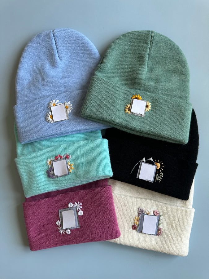 Knit beanies in blue, green, teal, maroon, ivory, and black with square embroidered patches
