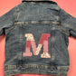 Denim jacket with red patchwork M applique and striped embroidery on the back
