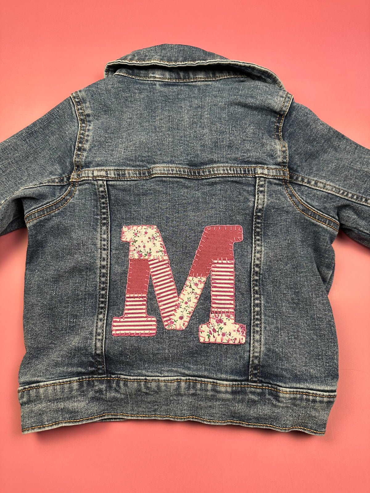 Denim jacket with red patchwork M applique and striped embroidery on the back