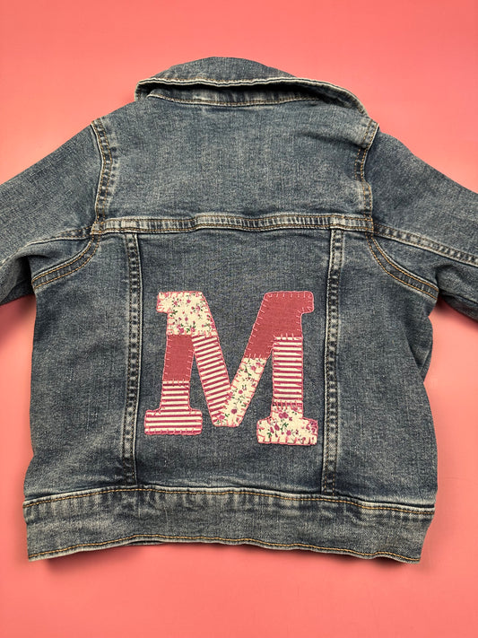 Denim jacket with red patchwork M applique and striped embroidery on the back