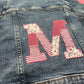 Denim jacket with red patchwork letter applique and striped embroidery on the back
