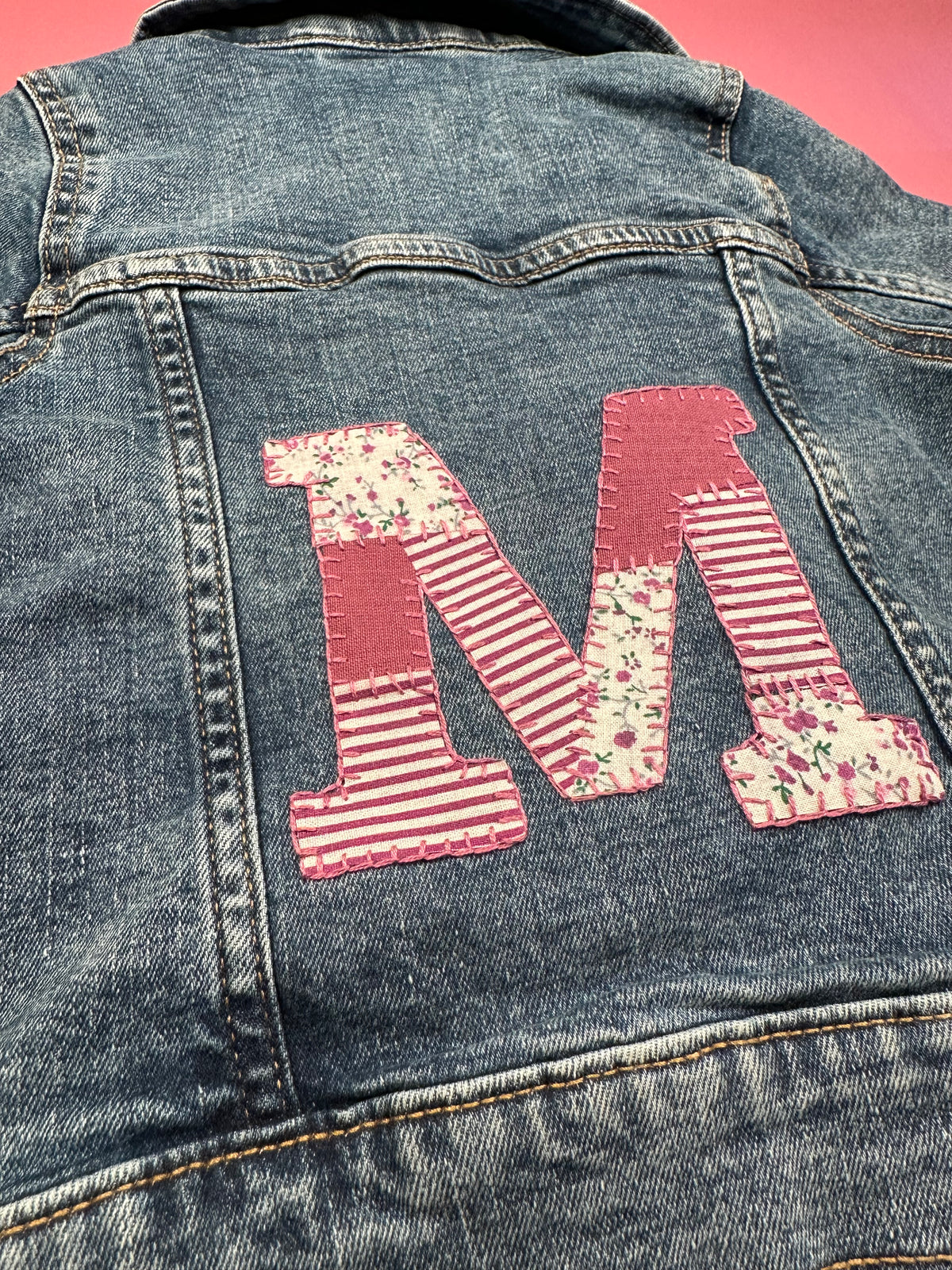 Denim jacket with red patchwork letter applique and striped embroidery on the back