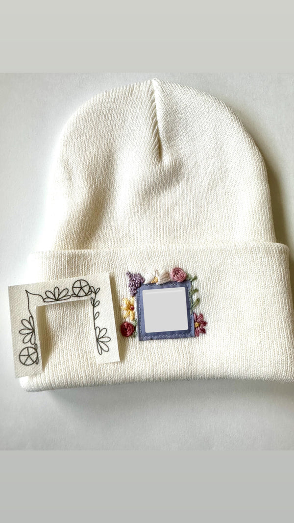 Off-white knit beanie with floral embroidery patch and small flower accents