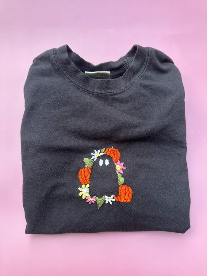 Dark gray sweatshirt with embroidered floral Halloween character centered on chest