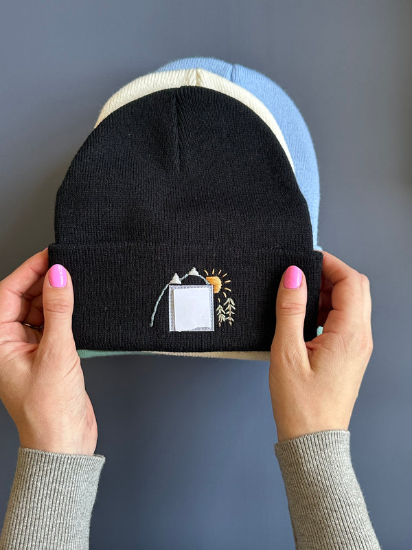 Black knit beanie with light blue cuff and small mountain sun embroidery patch