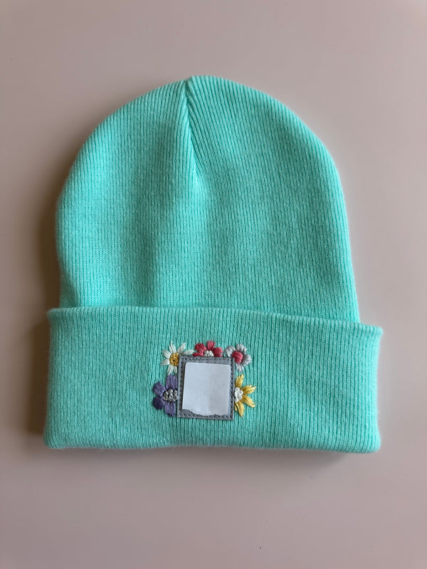 Turquoise knitted beanie with embroidered square patch and floral accents