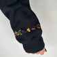 Dark hoodie sleeve cuff with multicolor cursive "boo" embroidery
