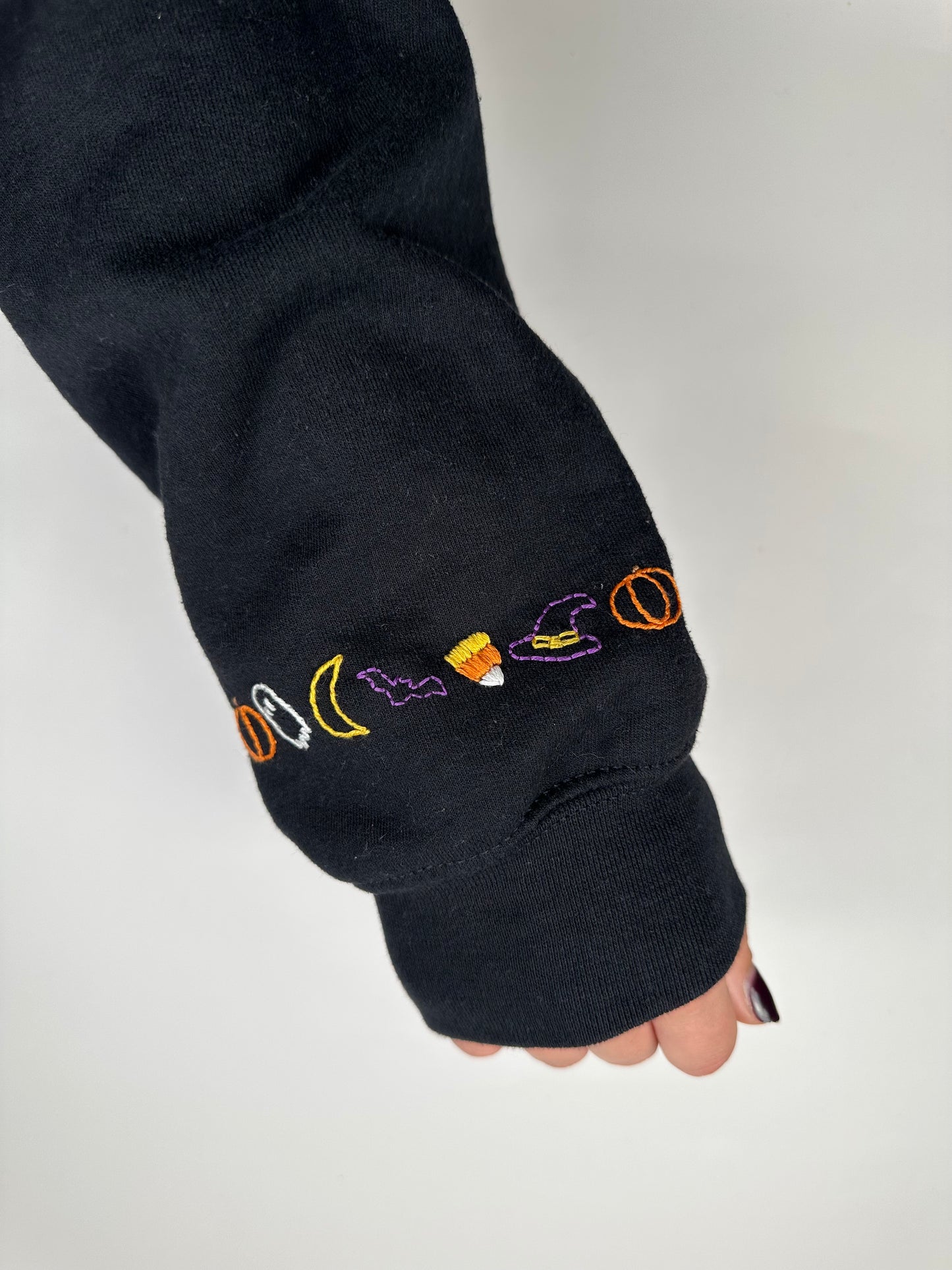 Dark hoodie sleeve cuff with multicolor cursive "boo" embroidery