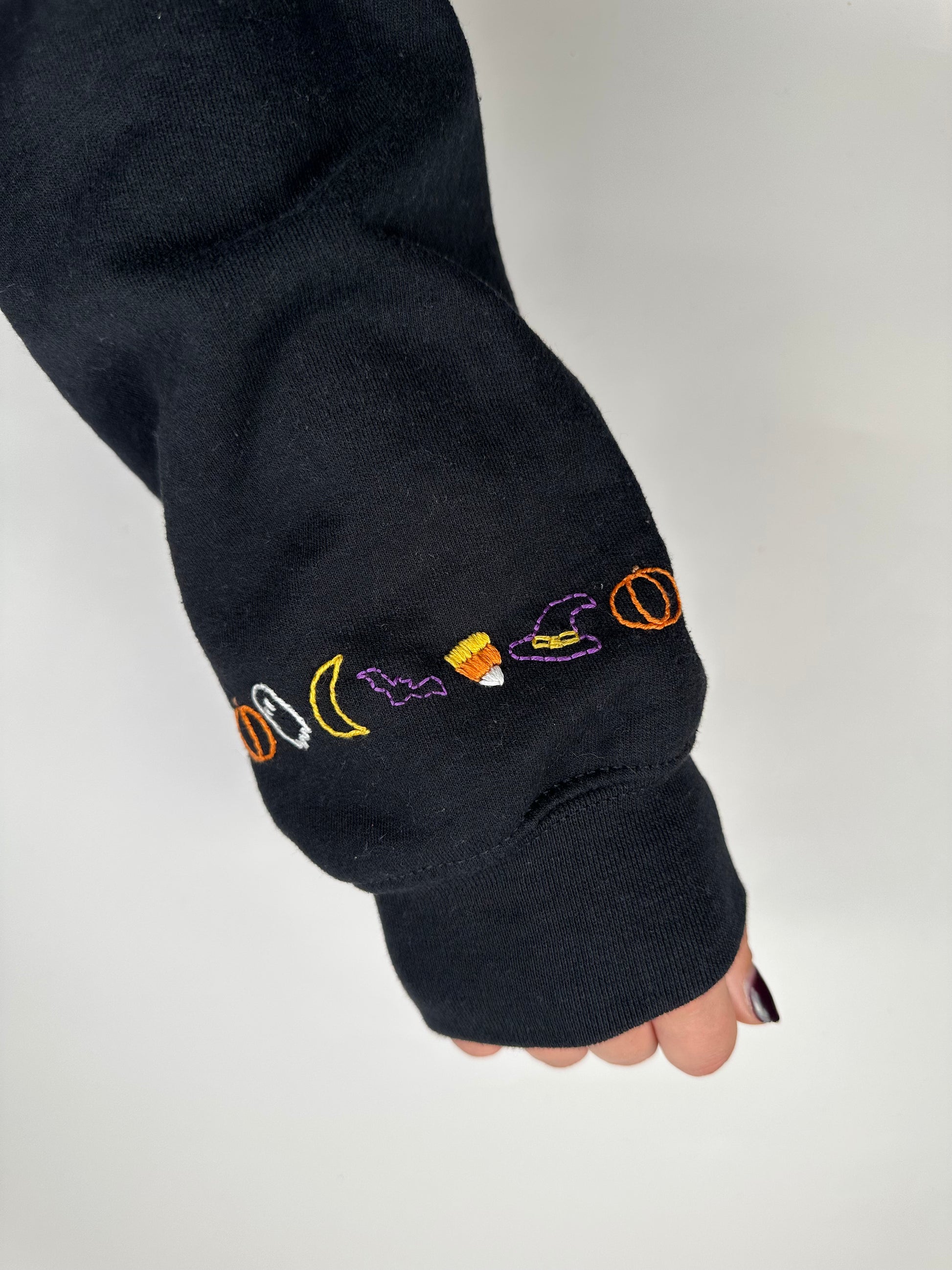 Dark hoodie sleeve cuff with multicolor cursive "boo" embroidery