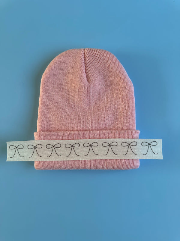 Pink knit beanie with ribbed cuff and black bow embroidery design strip