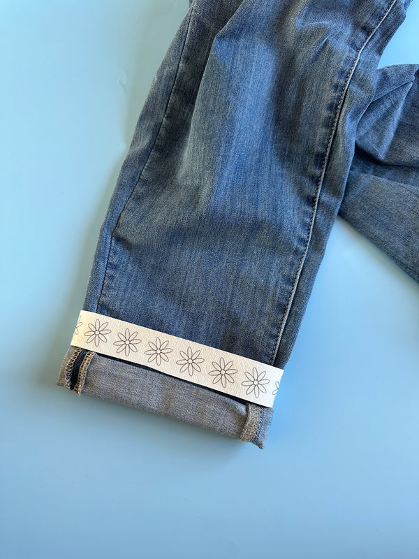Light blue denim jeans with white daisy embroidery detail along the hem edge